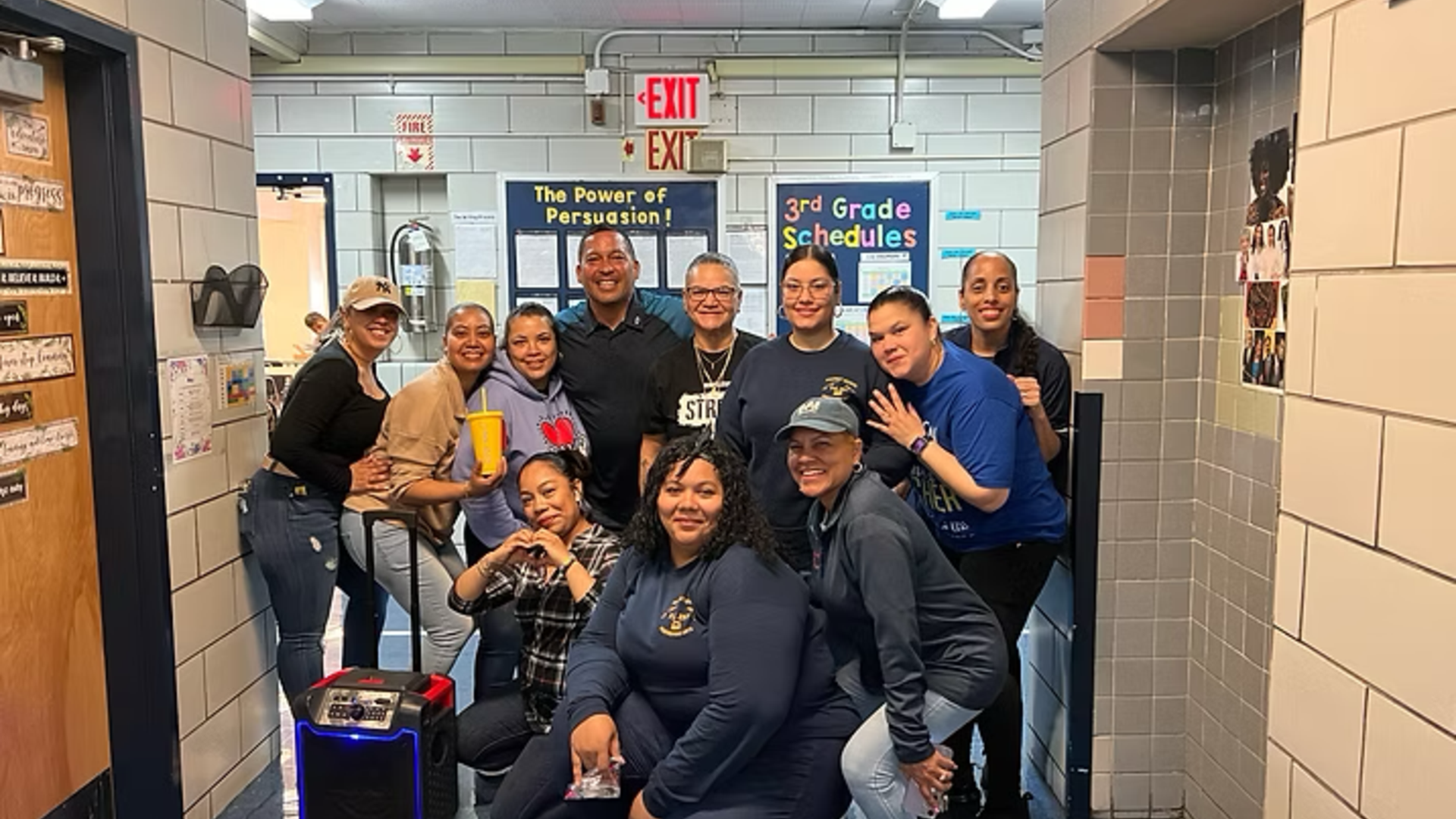 Group of smiling adults posing together in a school hallway.