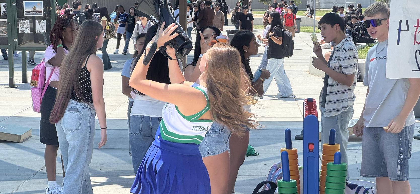 A cheerleader takes a selfie among a crowd at a bustling outdoor fair.