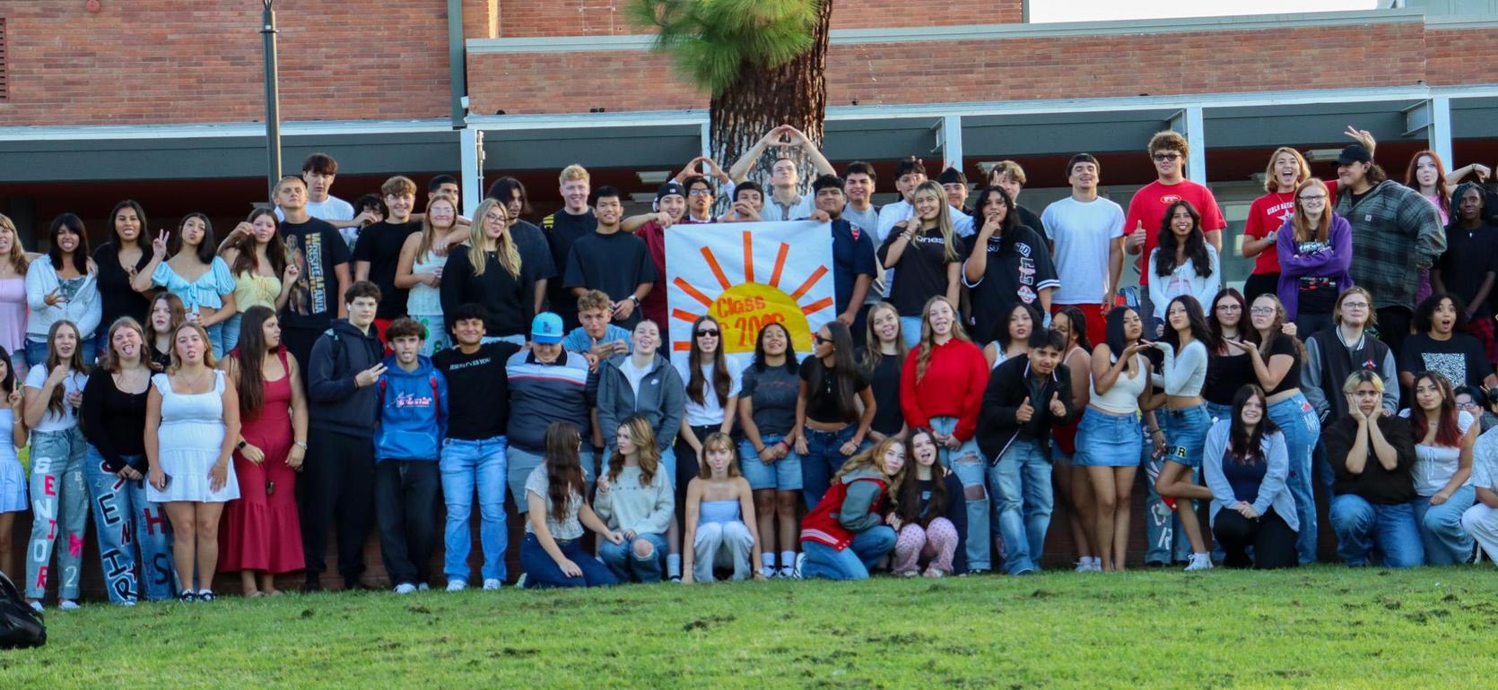 A large group of students posing together outdoors with a sun-themed banner.