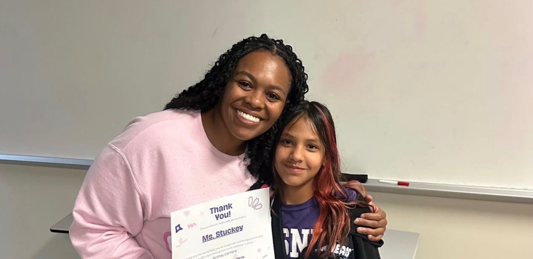 Two people smiling, one holding a certificate and a small gift.