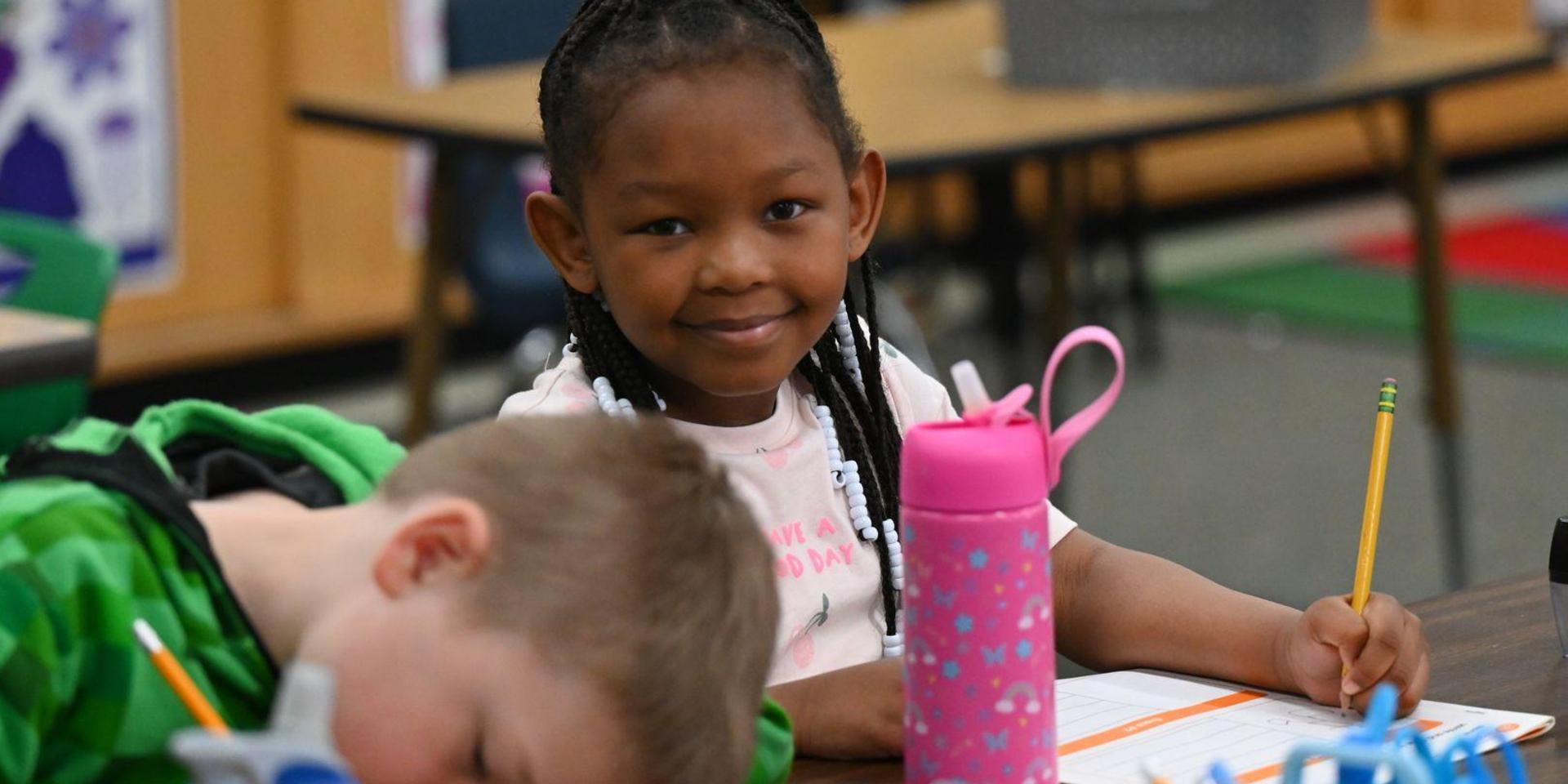 Girl smiling while working at a desk, boy resting his head down beside her.