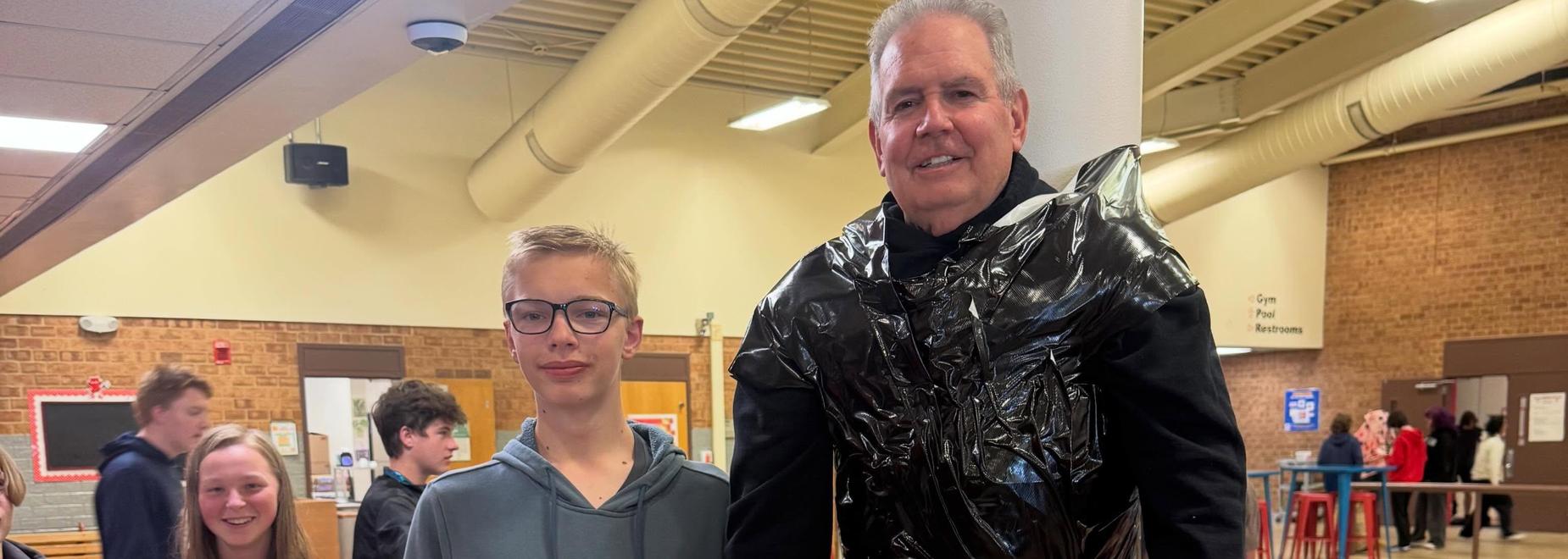 A group of students in a school setting, one wearing a garbage bag outfit.