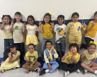 Group of children in yellow clothing posing and making peace signs.