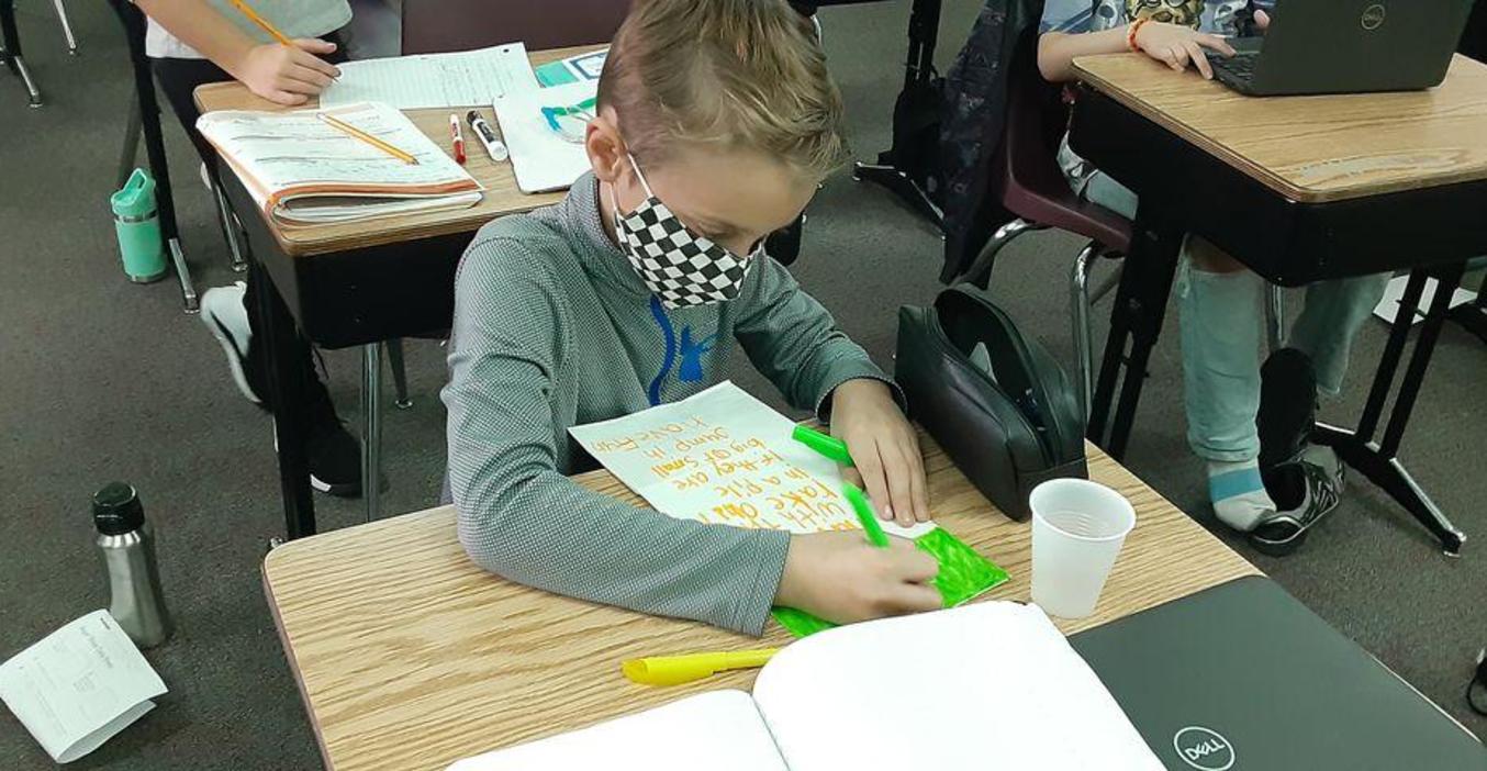 A Page student works on decorating a plain paper bag for Kids Food Basket.