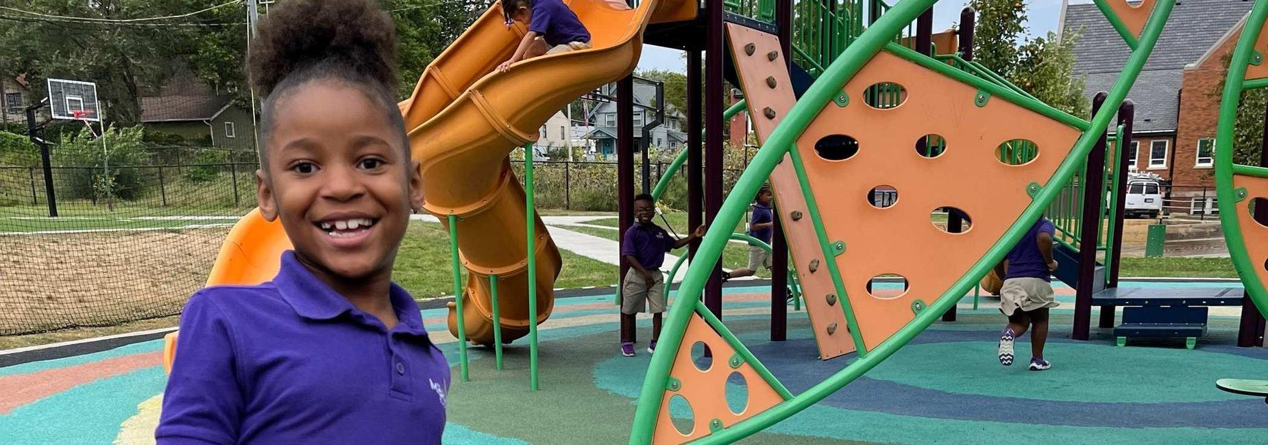 A scholar is pictured running and laughing on the playground while other children play behind them.