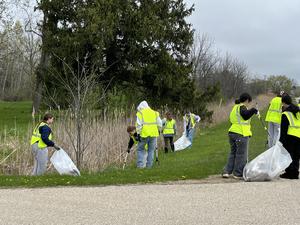 Volunteers cleaning up debris in a grassy area, carrying bags and tools.