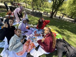 Five individuals sitting on a blanket, having a picnic and posing for the camera.