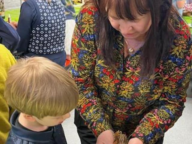 A woman shows a child a small animal while surrounded by other people in a colorful setting.