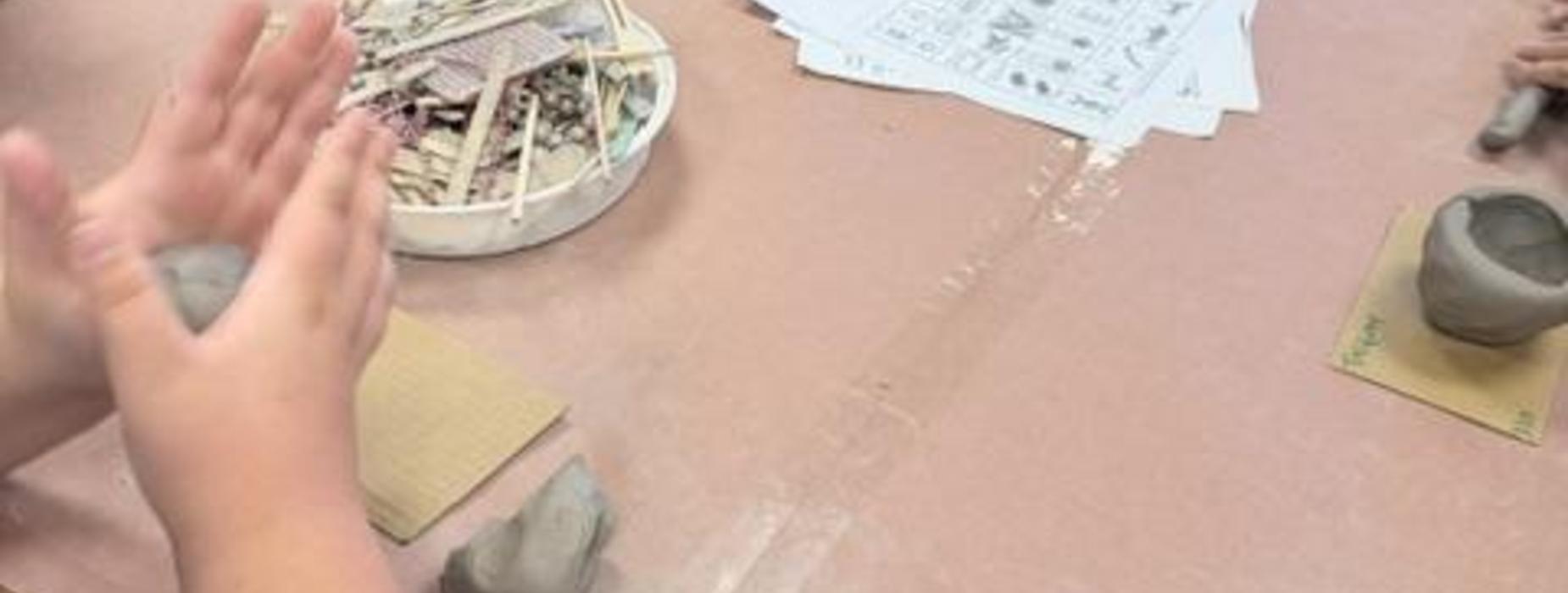 Hands mold clay while surrounded by crafting materials and instructions on the table.