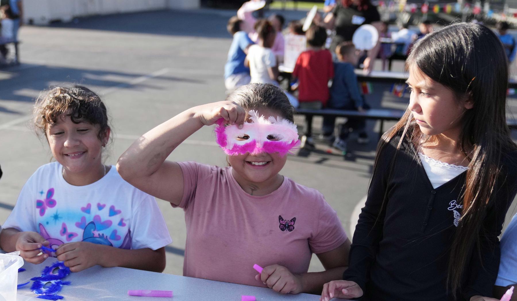 Student holding up a handmade mask with pink feathers