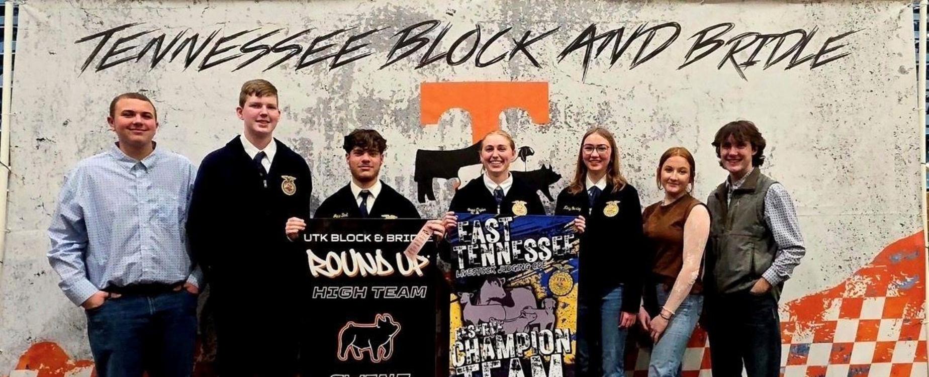 Seven members of a team hold banners celebrating their achievements together.