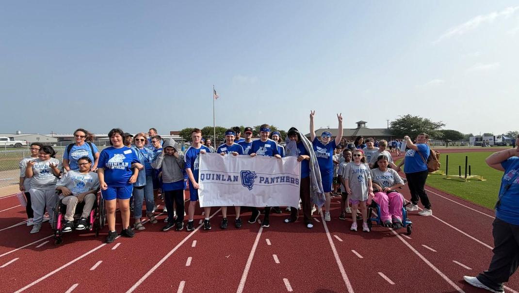 Group of people in blue shirts and a banner gathered on a track field.