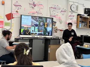 A student presents in front of a screen displaying various images and information.