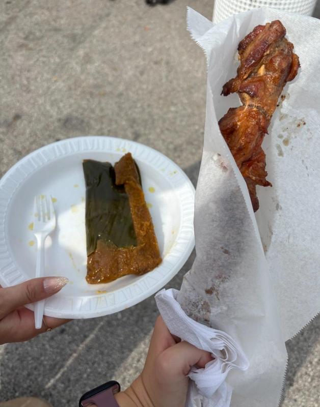 A plate with tamale wrapped in a banana leaf and grilled meat on a stick held by a person.