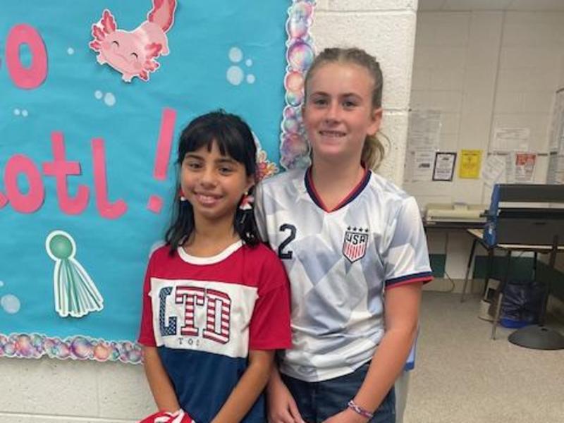 Two girls standing side by side, one in a red, white, and blue shirt and the other in a USA sports jersey.