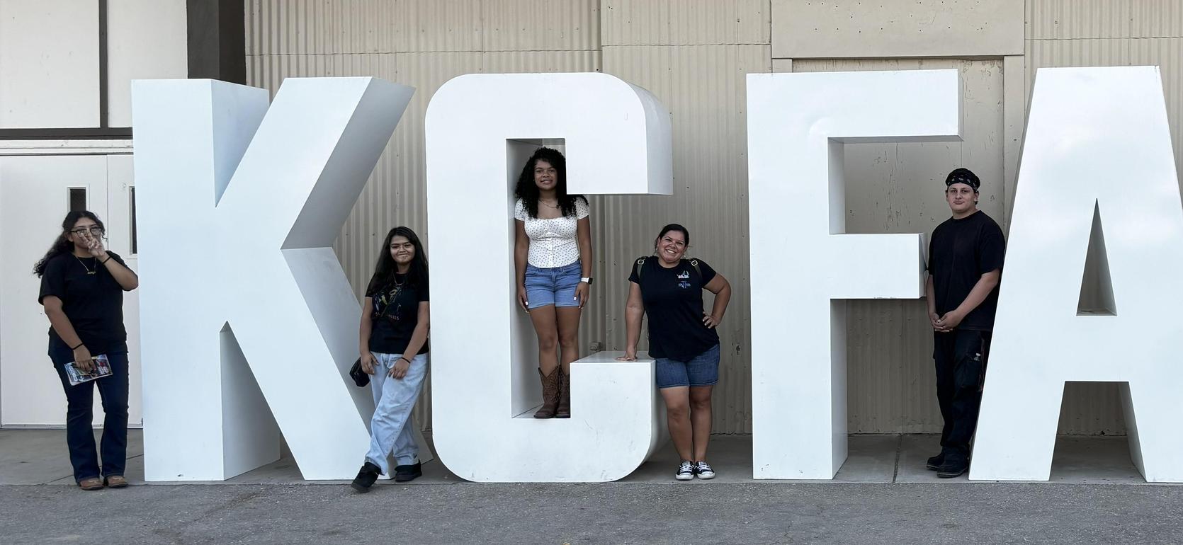 Group of six people posing beside large letters spelling 'KC FAIR'.