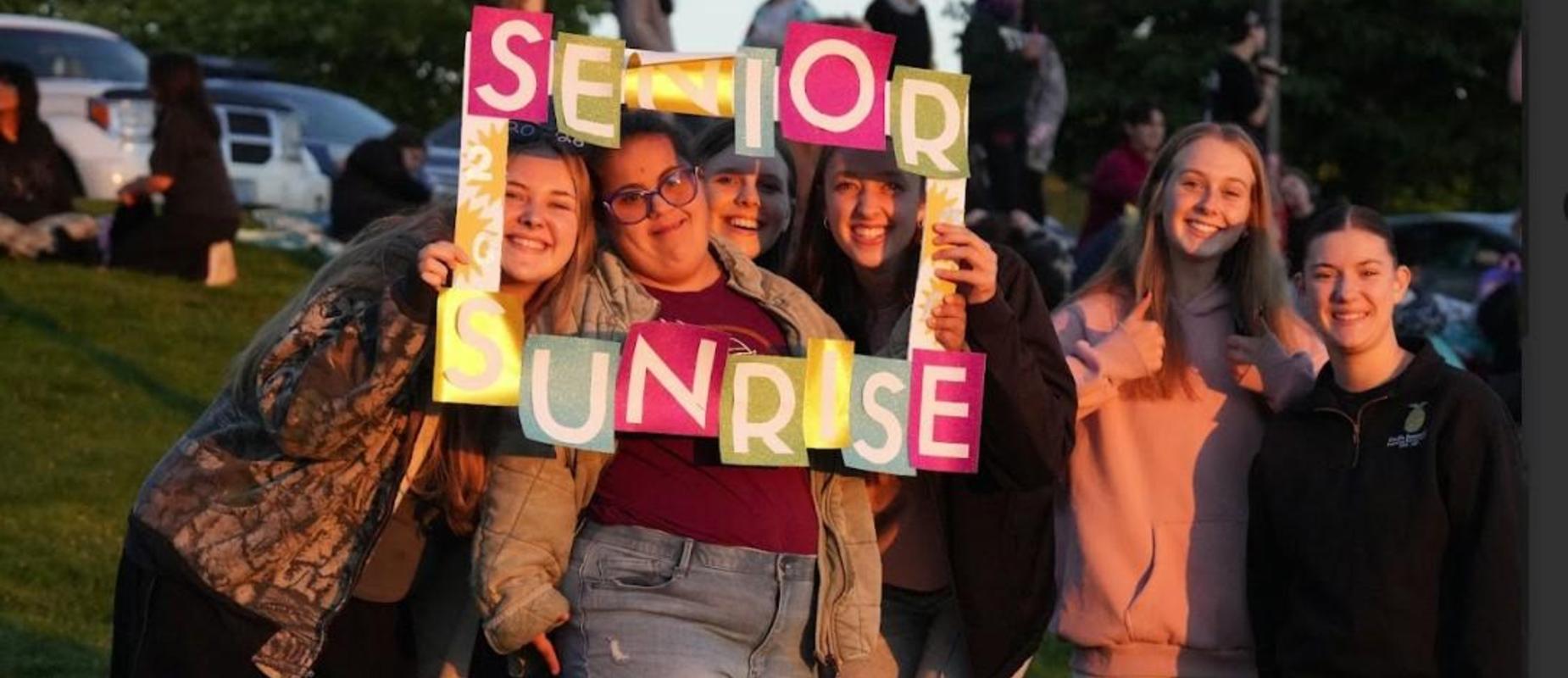 Group of students celebrating senior sunrise with colorful signs.