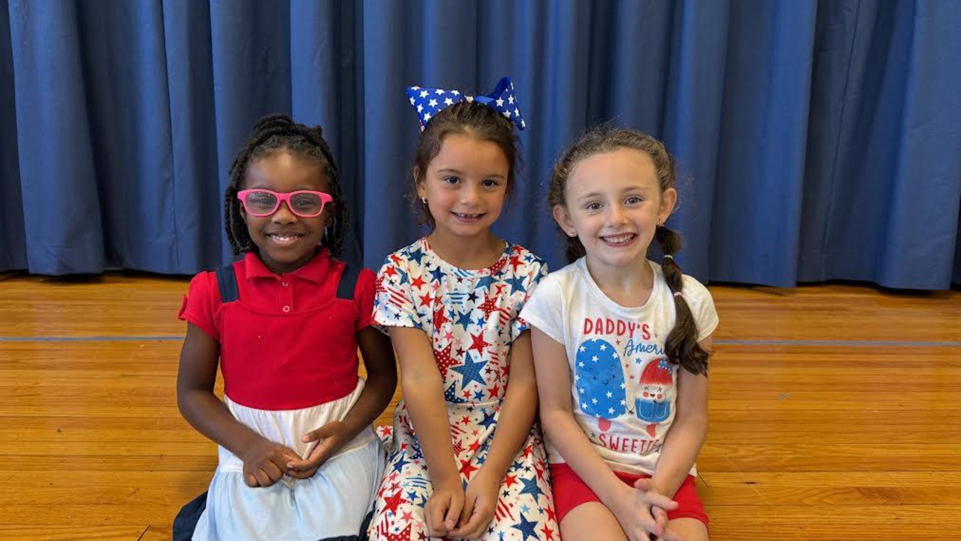 Three girls sitting together, smiling, wearing festive outfits and accessories.