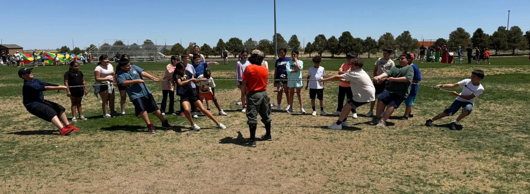 Group of teenagers participating in a tug-of-war on a sunny day outdoors.