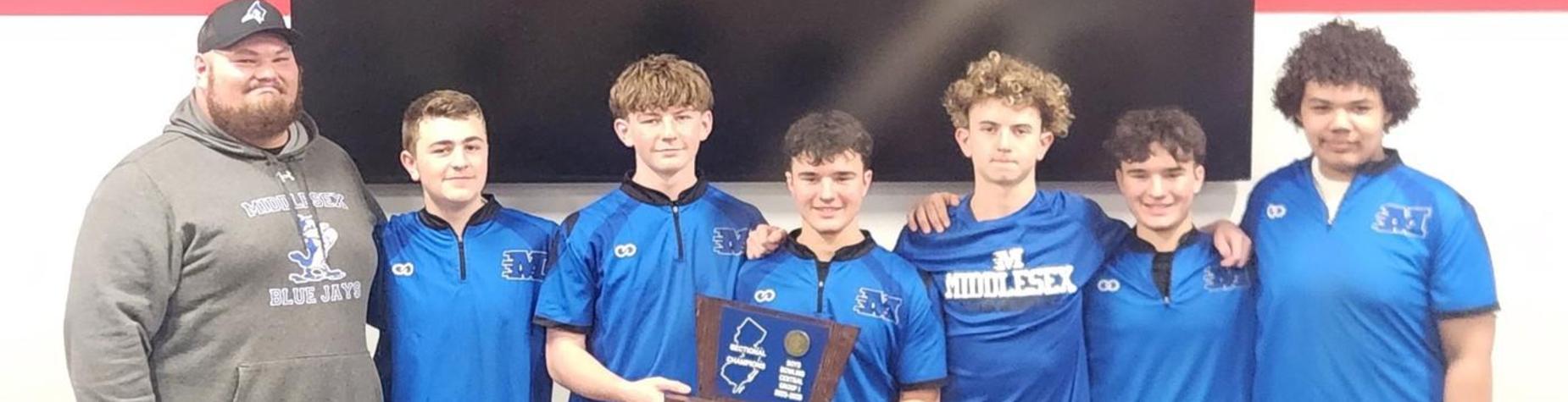 Group of six students in blue shirts posing with a coach.