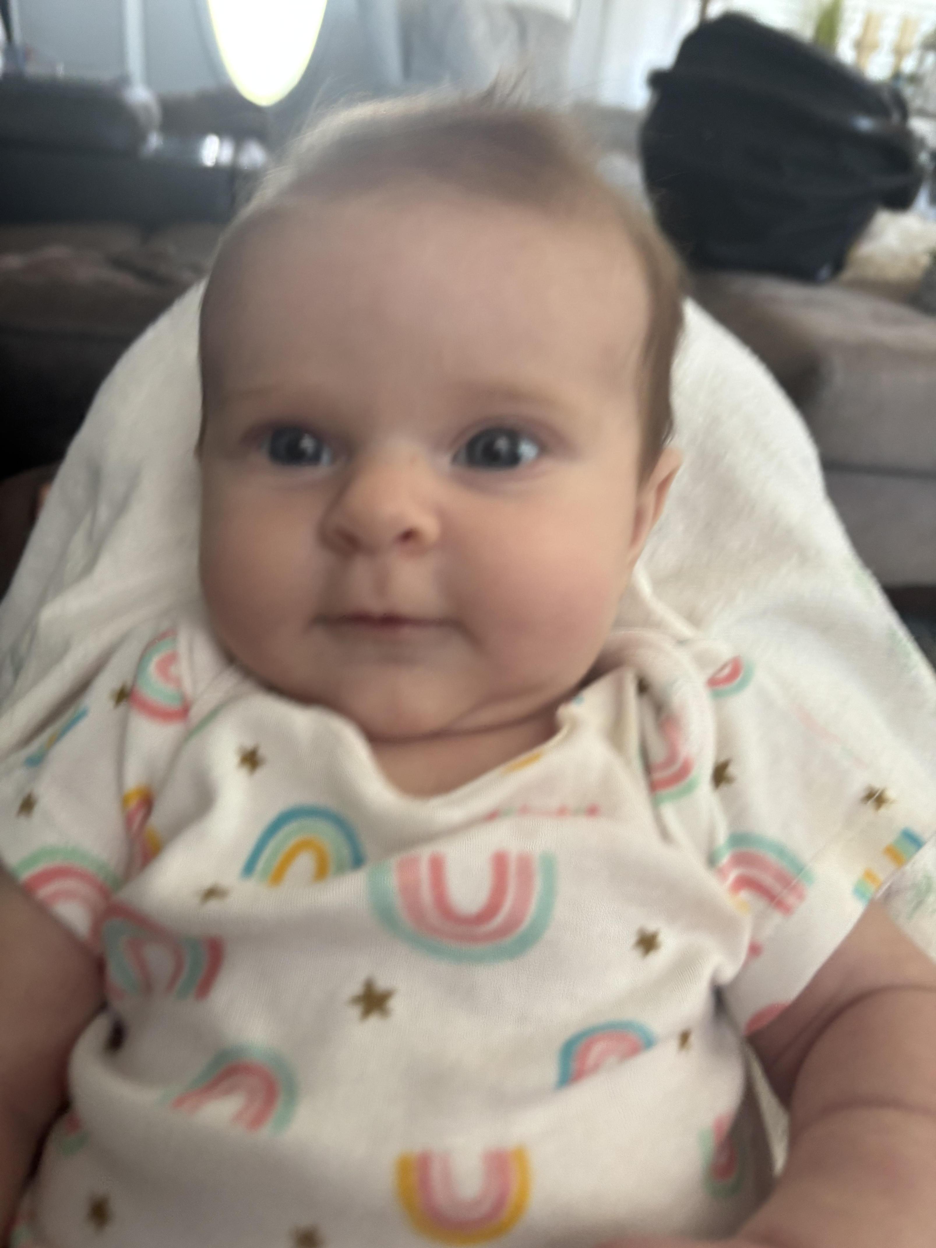 A close-up of a baby with a soft smile, wearing a colorful outfit.