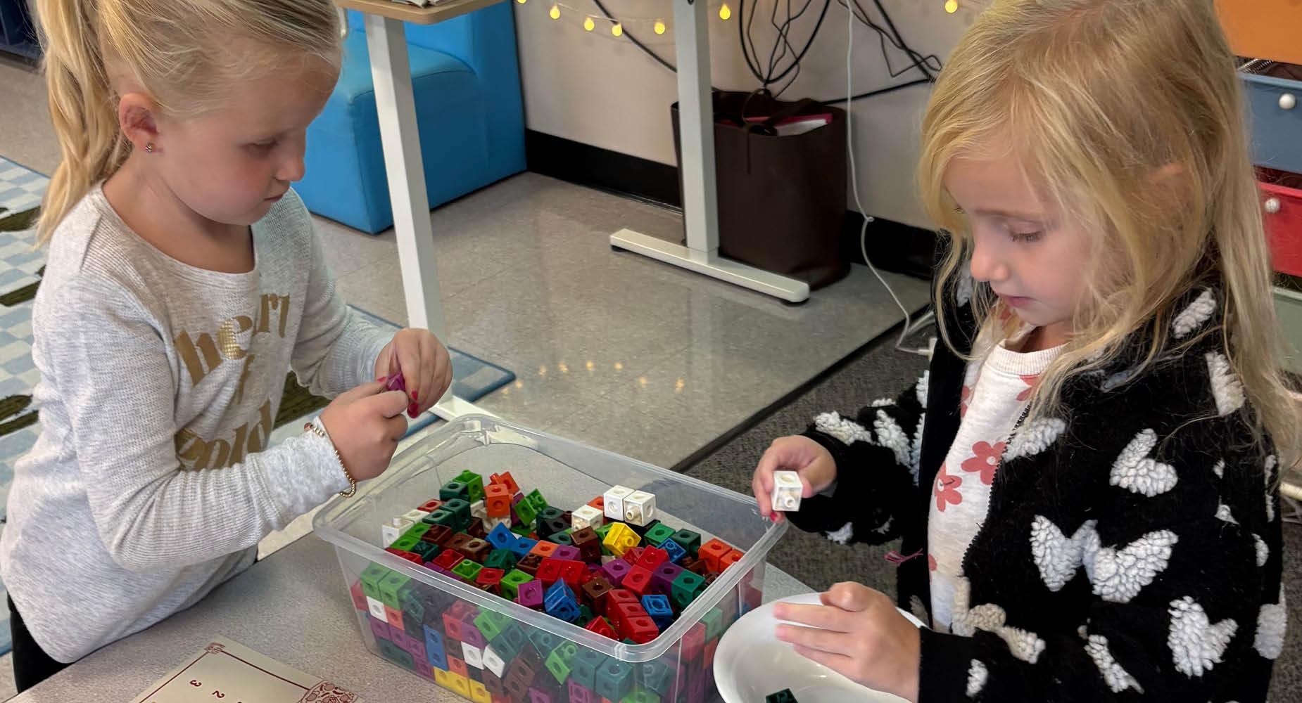 Two girls playing with colorful building blocks at a classroom table.