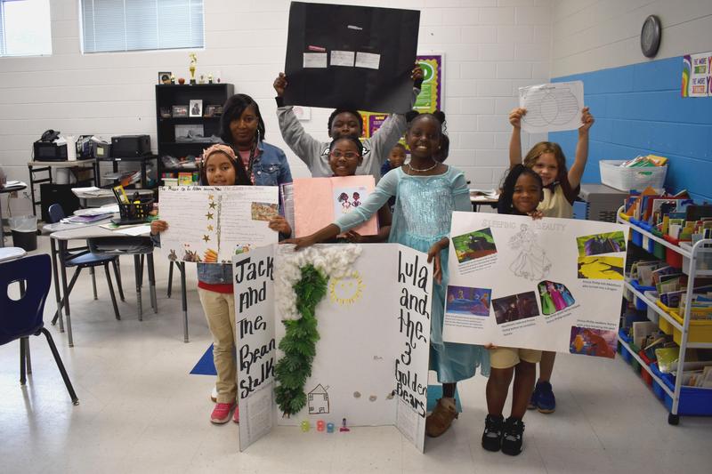 Third graders are standing holding research projects they did about tales from other countries.