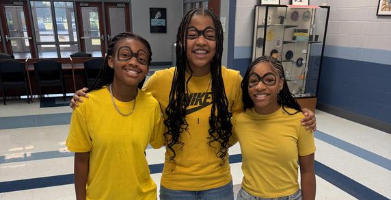 Three individuals wearing yellow shirts and denim shorts smile together indoors.