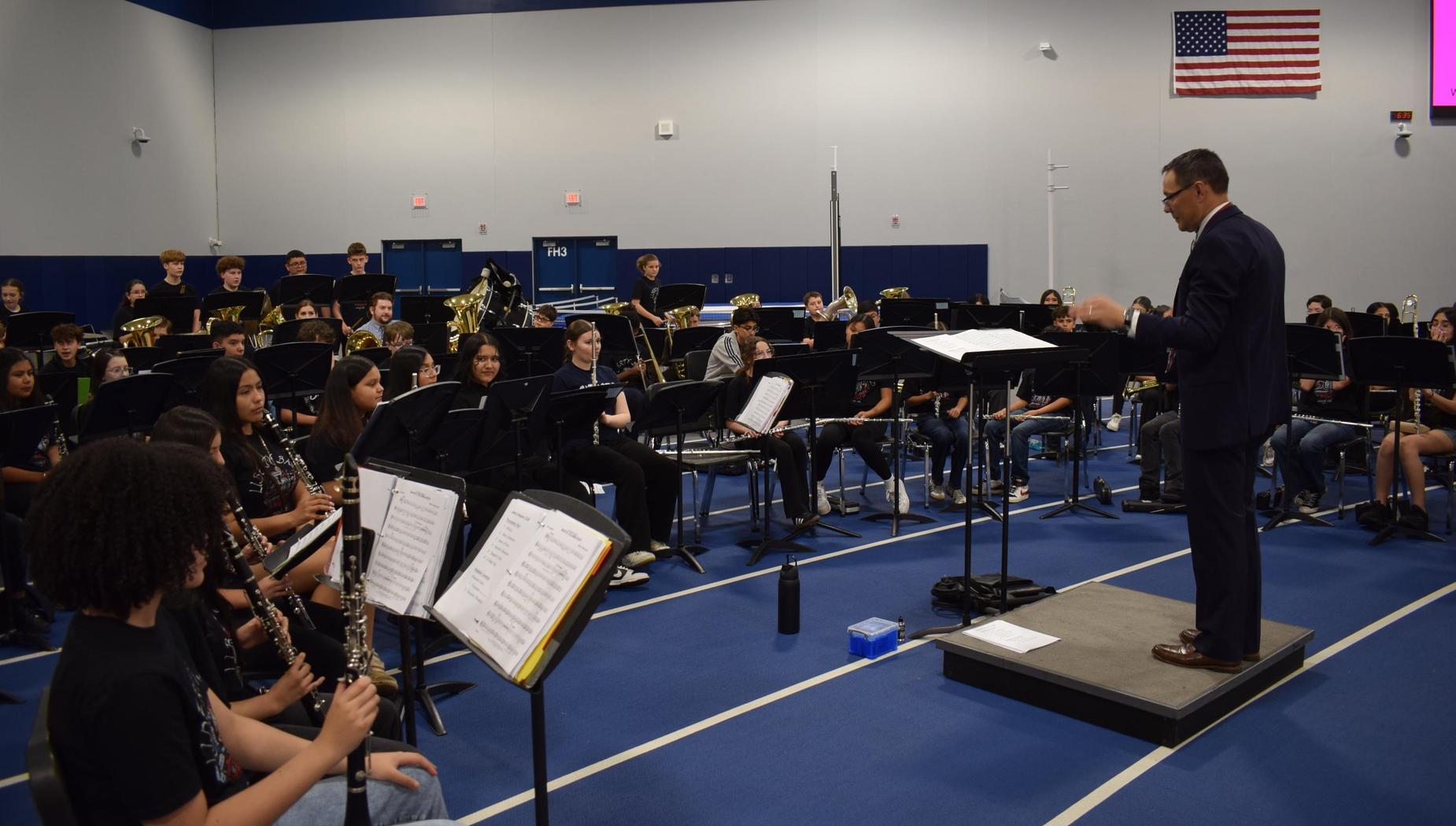 A band performs under a conductor in a gymnasium setting.