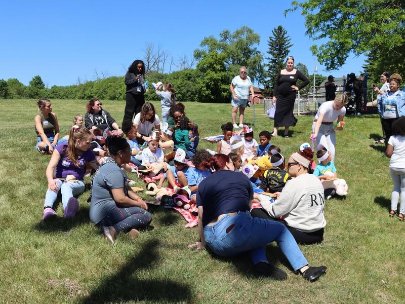 Group of children and adults sitting on grass at an outdoor event.