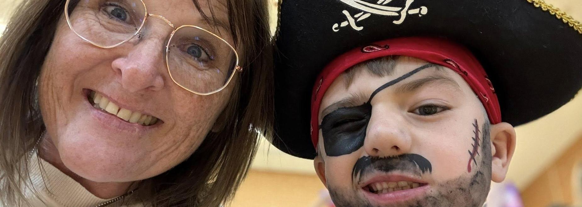 A smiling woman and a child dressed as a pirate with face paint and a hat.