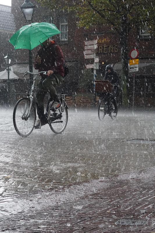 Cyclists riding in heavy rain, one with an umbrella and the other on a bike.