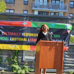 A woman speaking at a podium in front of a colorful banner about leadership.