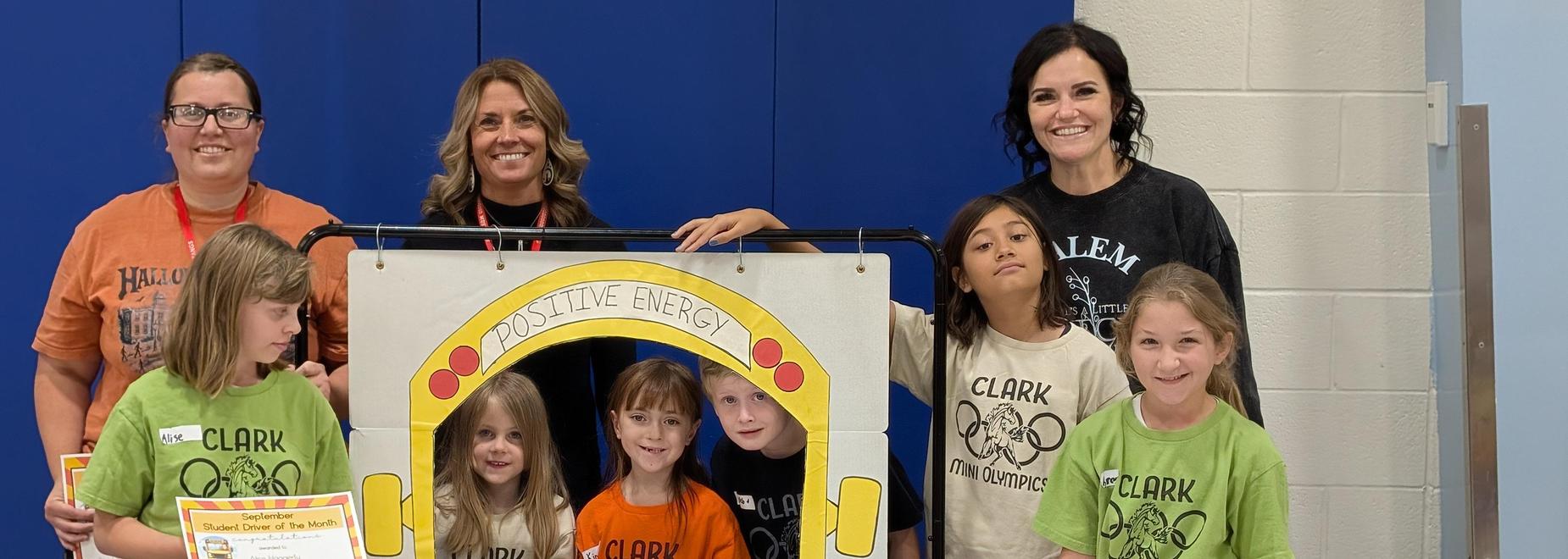 Group of children and adults holding up a sign that reads 'Positive Energy' in a school setting.