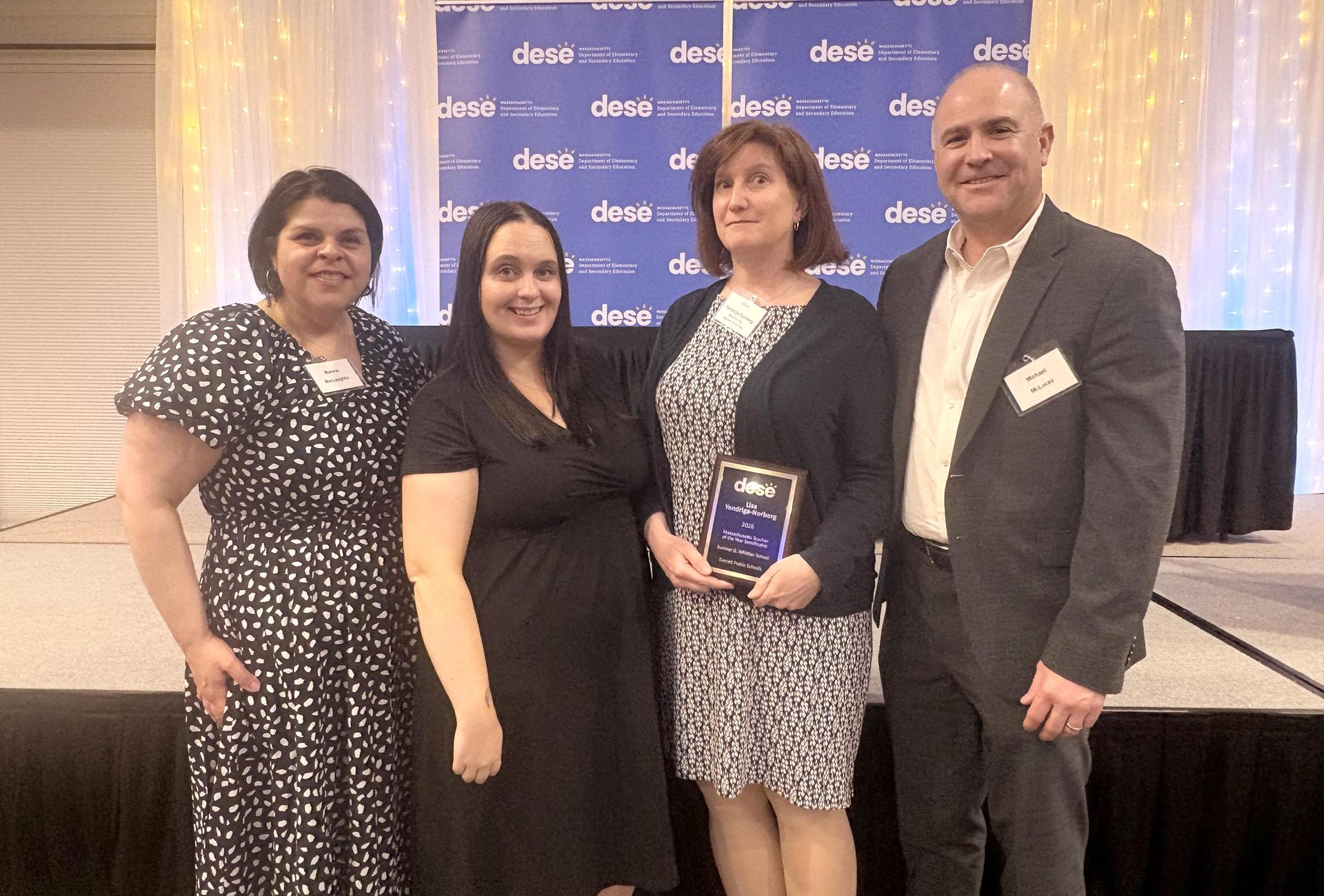 Four professionals holding an award in front of a decorated backdrop.