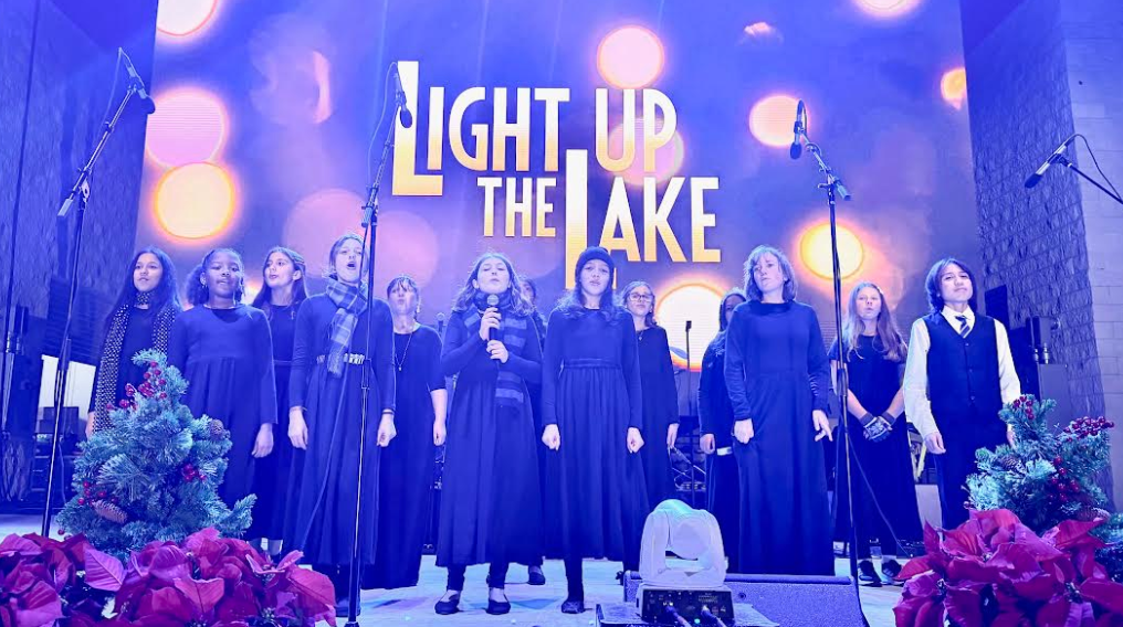 Honor Choir sings in black dresses and a black suit on a stage with poinsettia flowers.