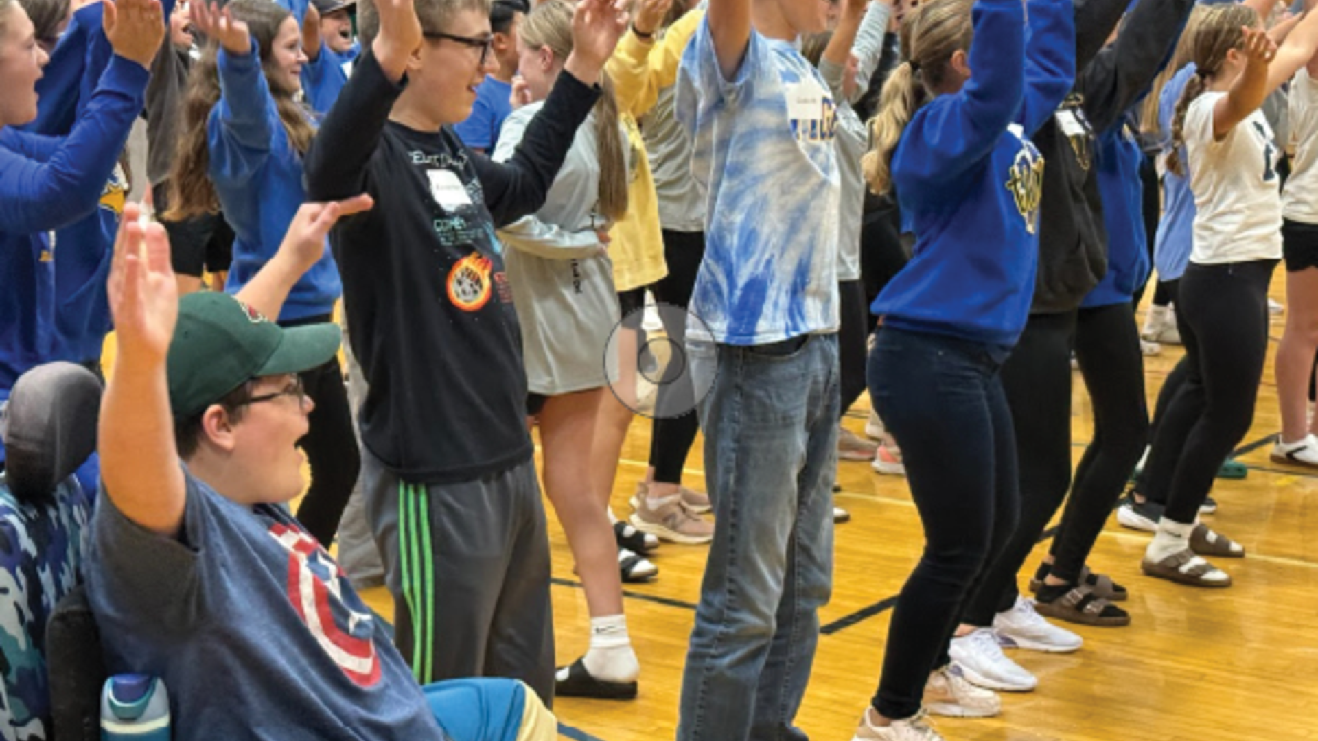 Participants joyfully dancing with arms raised in a gymnasium during an event.