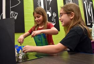 Two girls are engaged in a craft project at a table with colorful backgrounds.