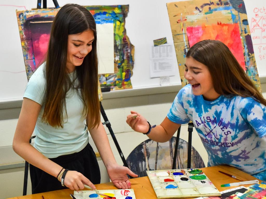 Two students smiling and painting in the art room.