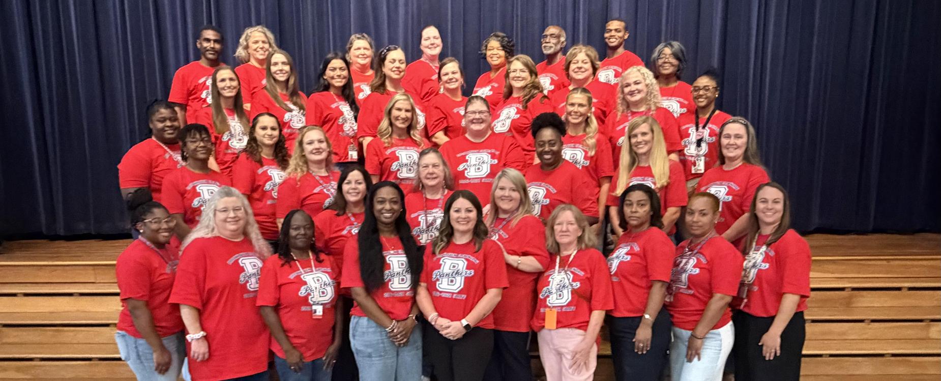 A large group of people wearing red shirts posing together on a stage.
