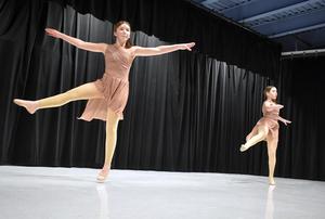 Two girls in pink outfits dancing on stage.