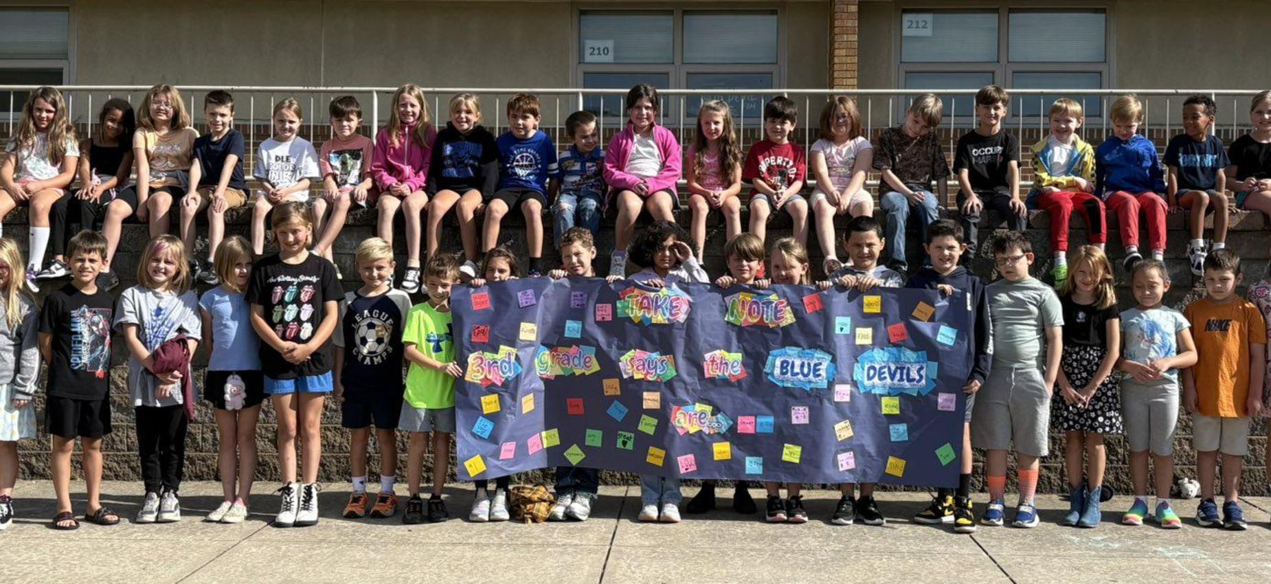 3rd grade ready for Elementary Night at the football game. Their sign reads "Take Note- 3rd grade says the Blue Devils are:" and each Post-It note lists something different.