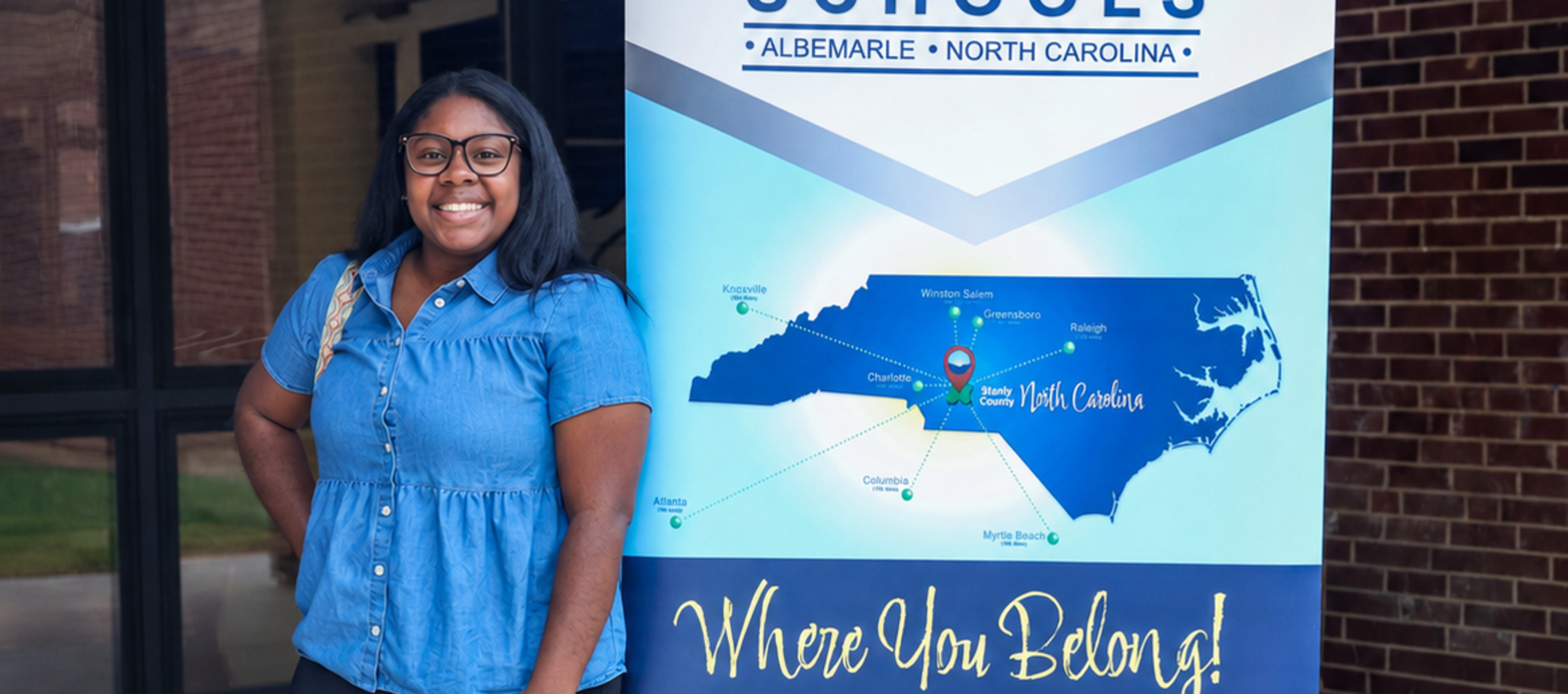 A woman in a denim shirt stands beside a banner with a map of North Carolina.