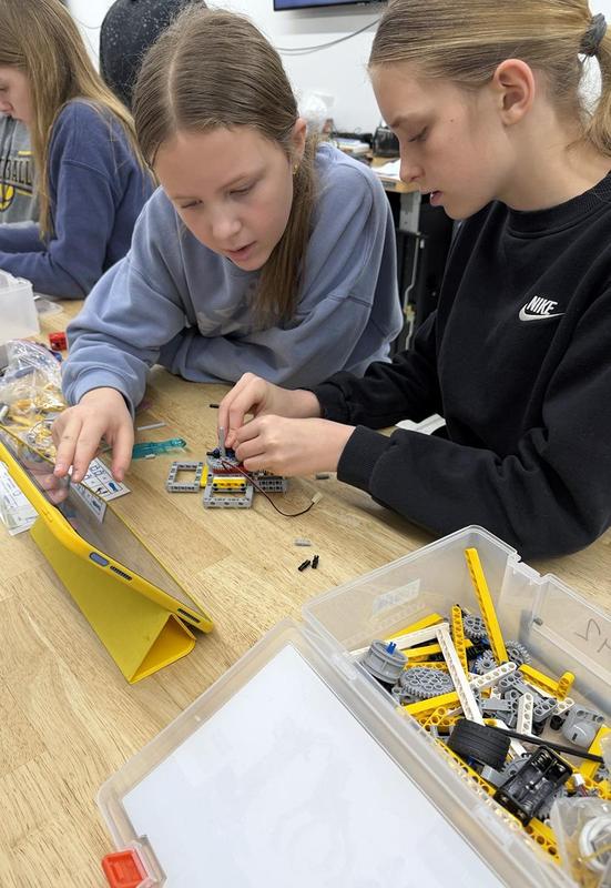 two girls building legos while working on a tablet computer
