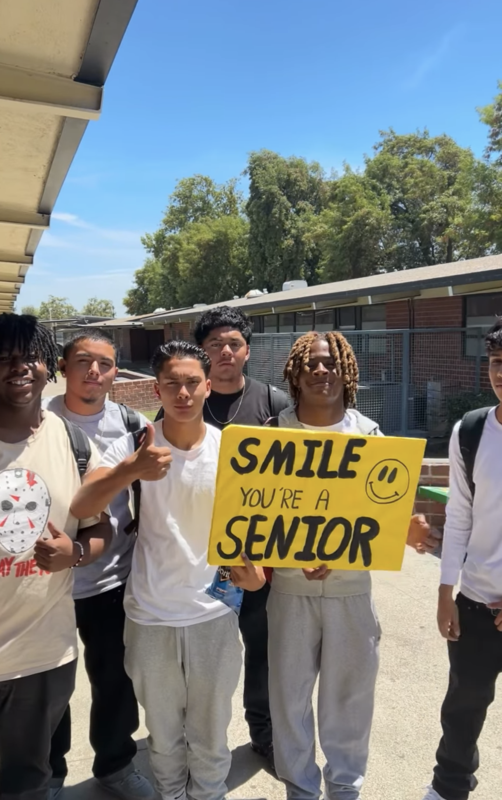 Six students in between classes put up a yellow sign that says Smile You're a Senior