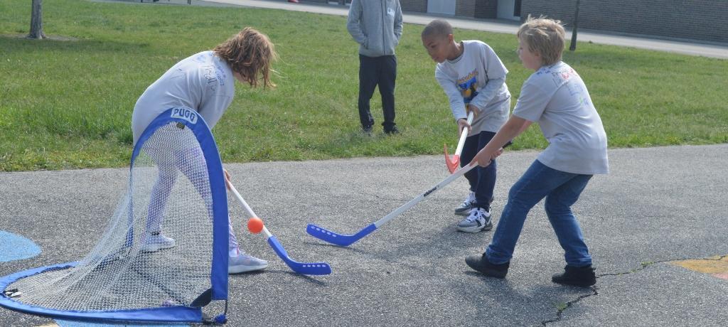 three students play field hockey