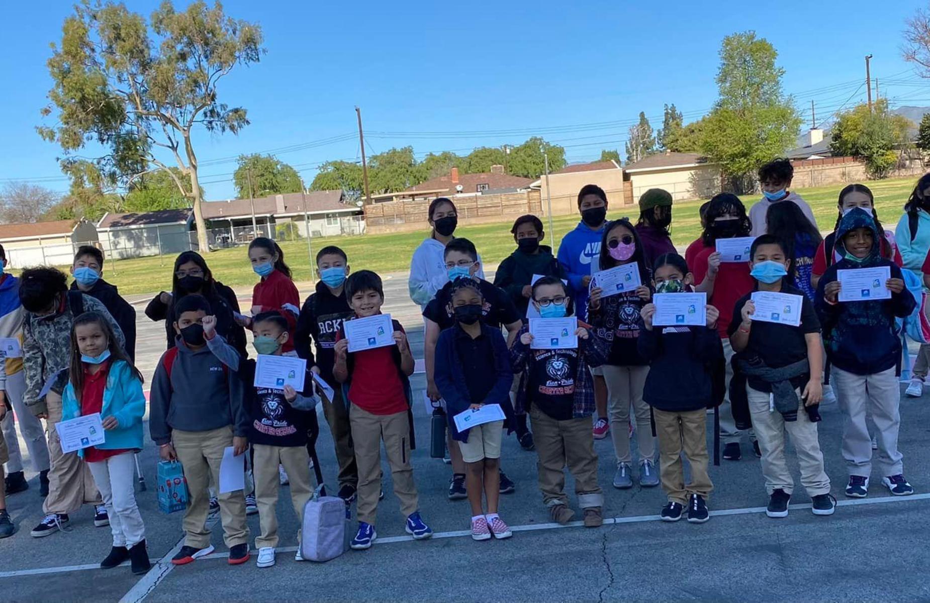 student achievers showing their certificates in a shaded area of the playground