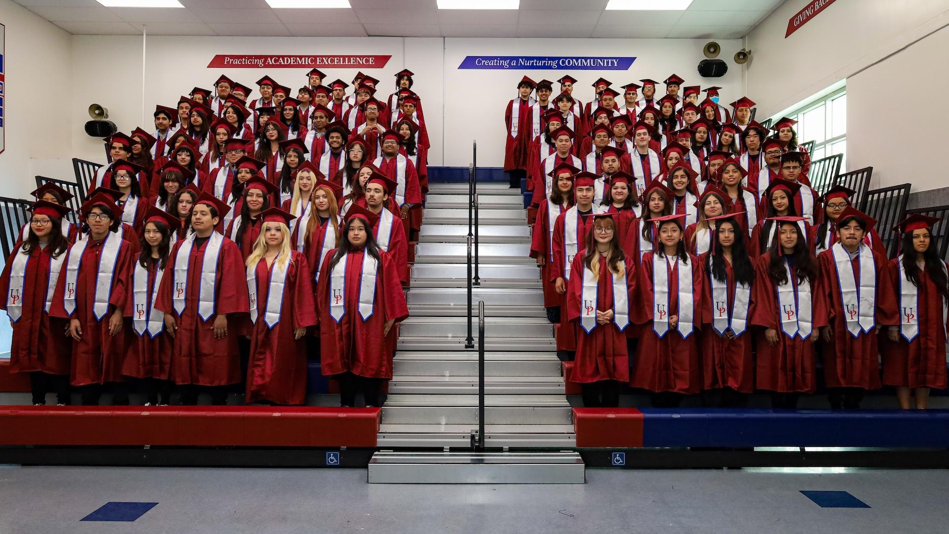 A large group of graduates in caps and gowns arranged on bleachers.