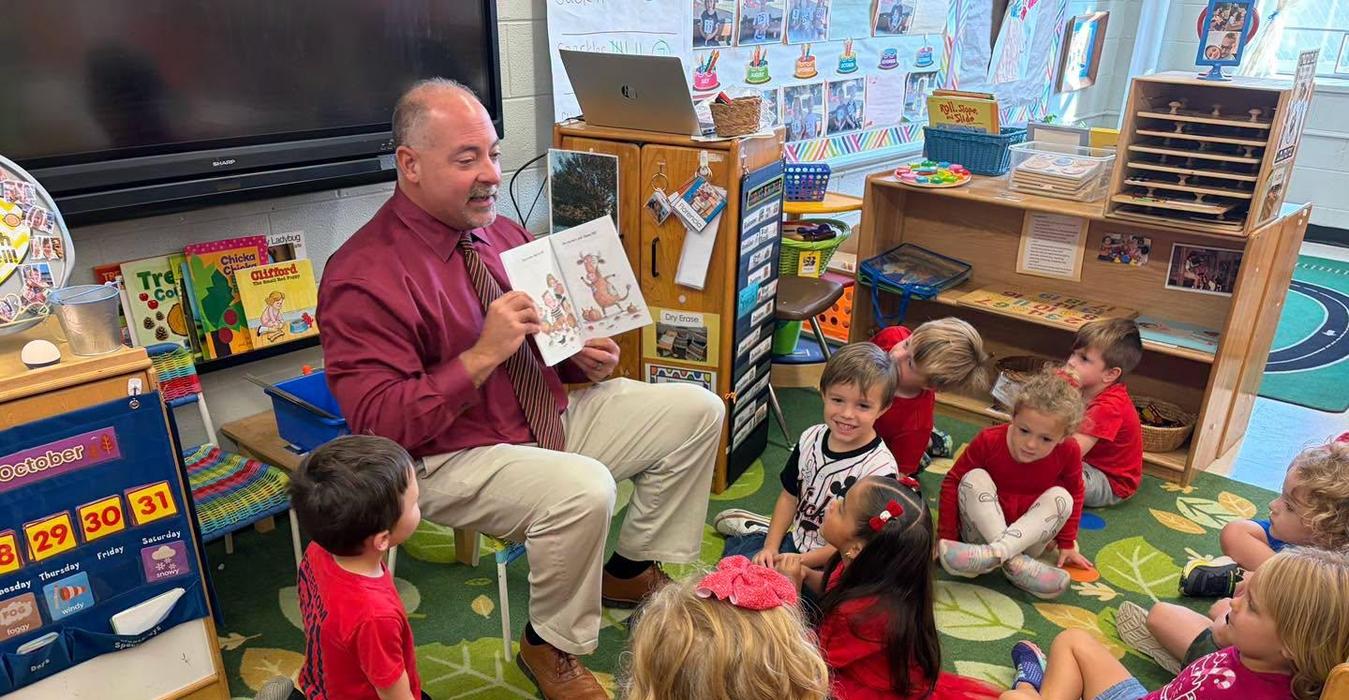 A teacher reading to a group of children sitting on a colorful carpet.