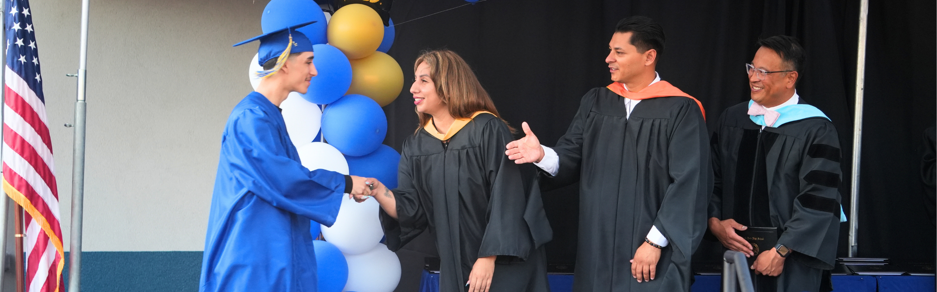 A graduate shakes hands with officials in caps and gowns at a graduation event.